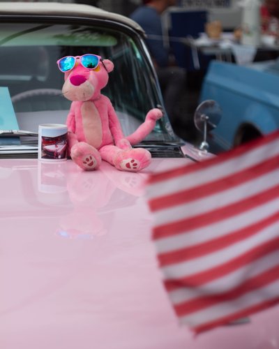 Pink Panther plush displayed on a classic American car hood at a vintage automotive event