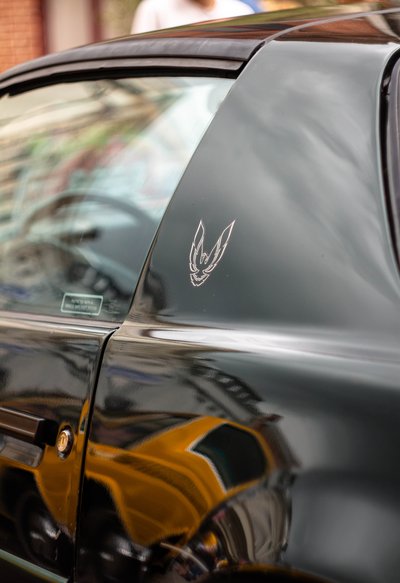 Close-up detail of a black Pontiac Firebird Trans Am emblem with glossy reflections and cinematic lighting