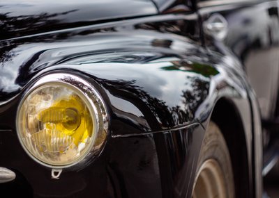 Close-up portrait of a black vintage Citroën with yellow headlights and glossy retro bodywork reflections